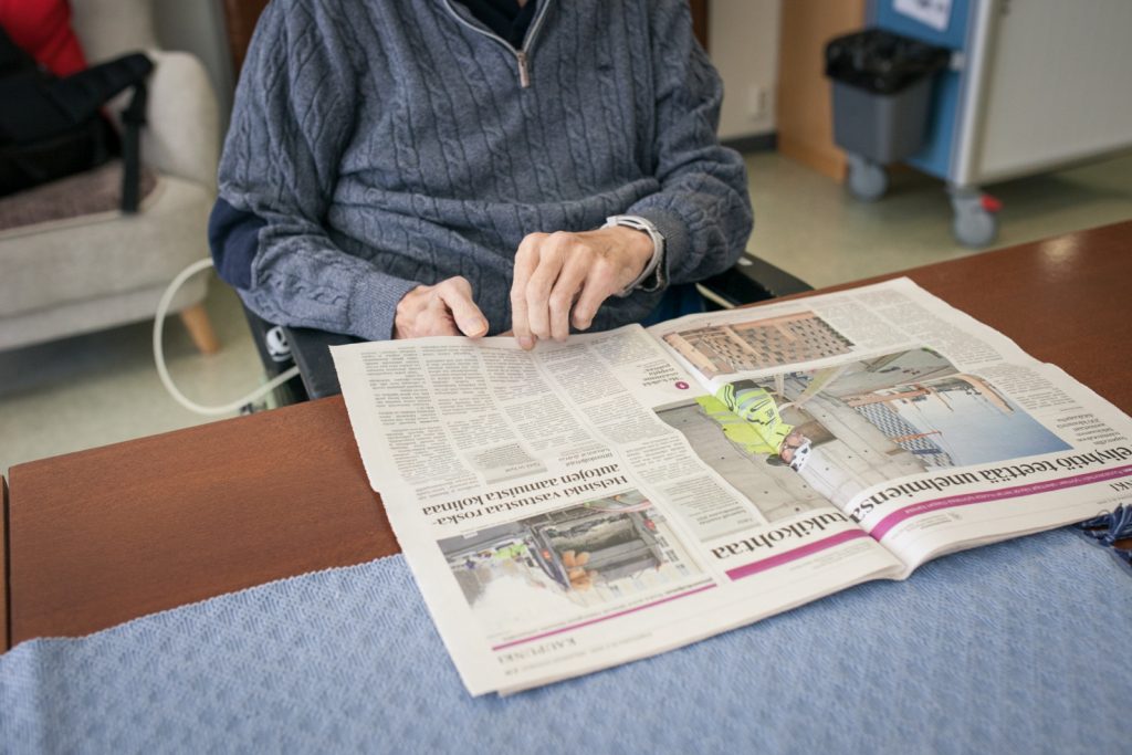 Vanha henkilö lukee sanomalehteä pöydän ääressä.