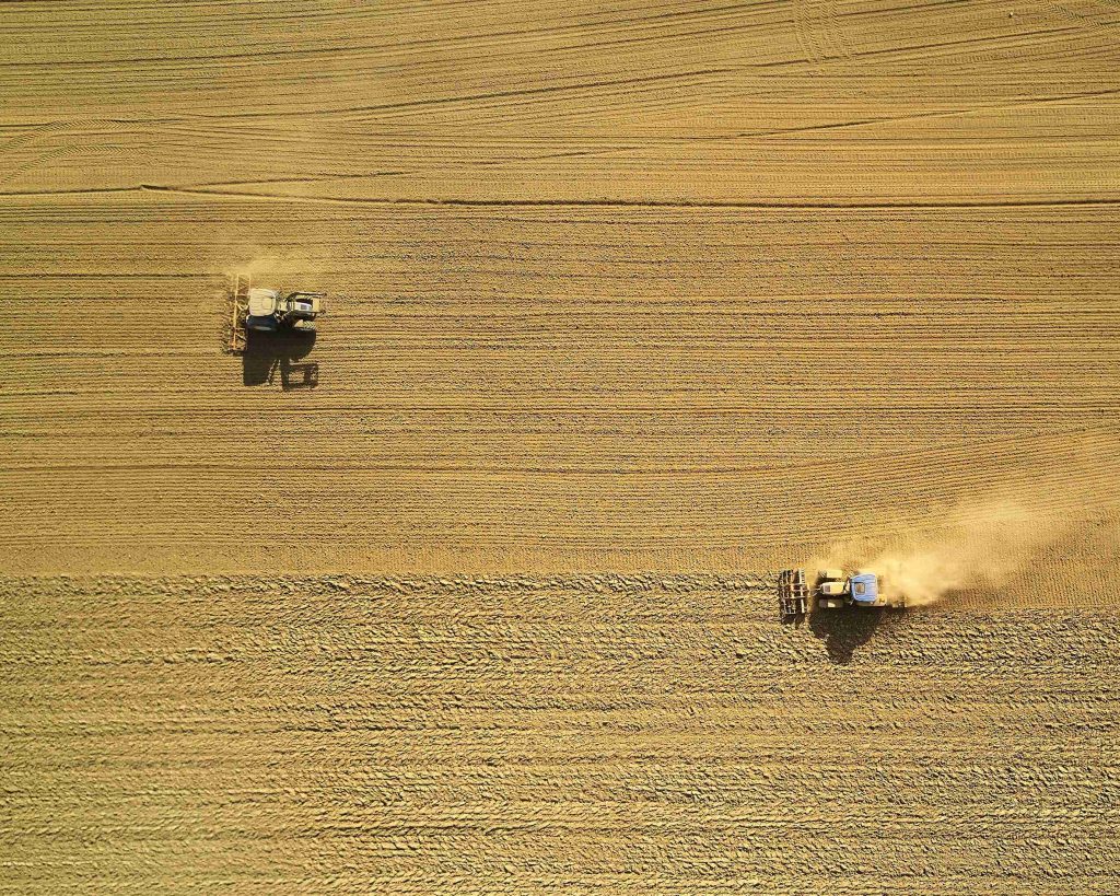 Vaaleanruskea pelto, jolla kulkee kaksi traktoria, ylhäältä kuvattuna.