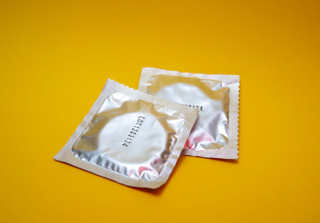 Kaksi kondomipakkausta keltaisella tasolla.