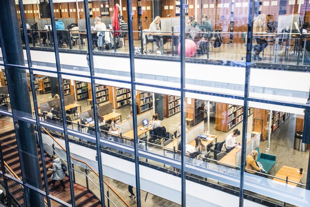 Kolme kerrosta kirjastoa, jossa on lukuisia ihmisiä työskentelemässä, kuvattuna ulkoapäin.