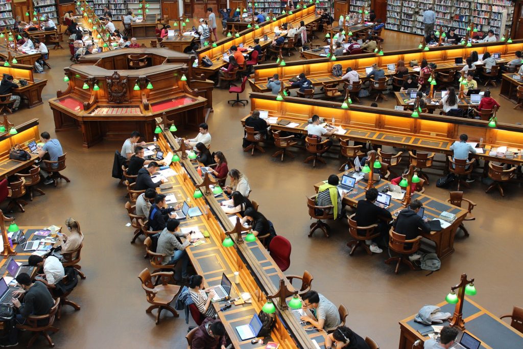 Lukuisia ihmisiä läppäreiden ääressä isossa kirjastosalissa.