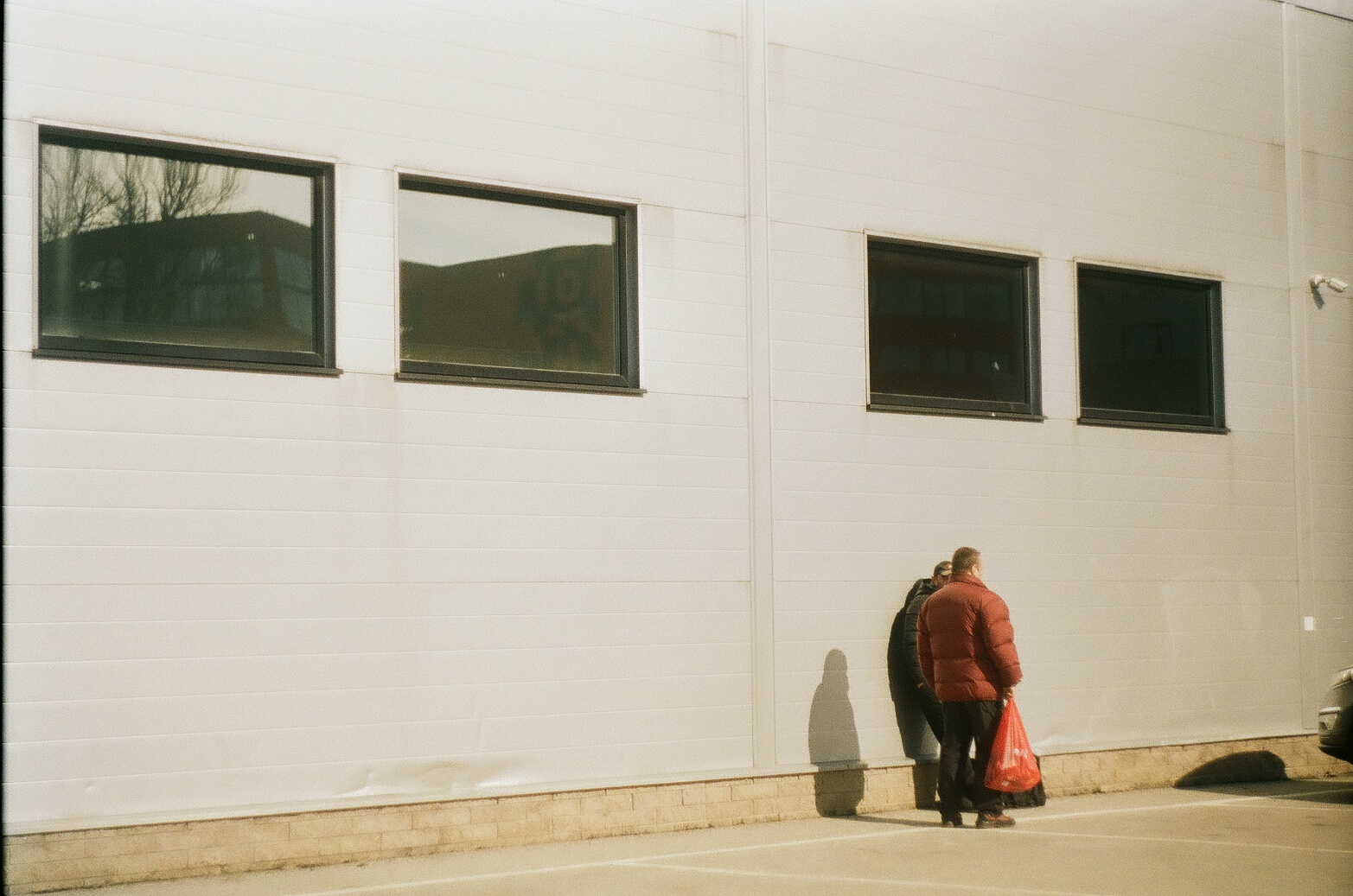 Kaksi ihmistä juttelee ison teollisuusrakennuksen edessä selin kameraan