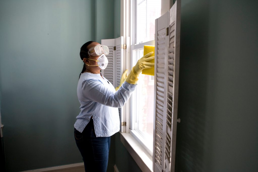 Maskilla ja suojalaseilla varustautunut siivooja pesee ikkunoita.