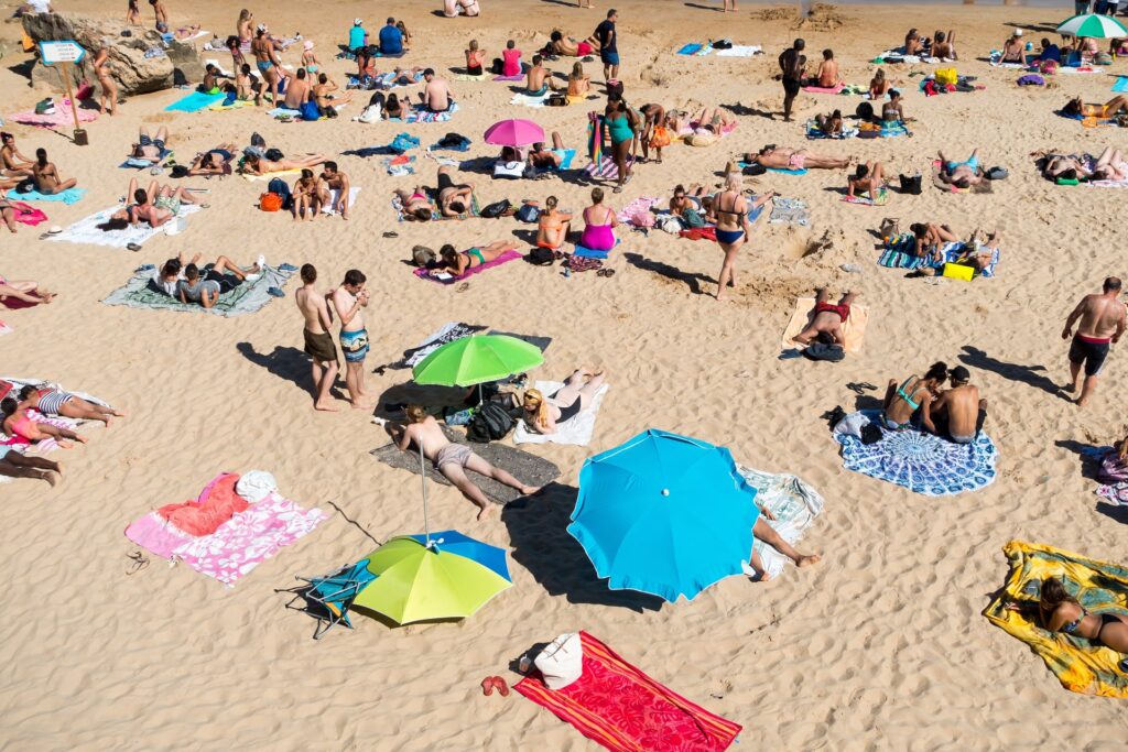 Ihmisiä hiekkarannalla. Kuvassa näkyy useita eri värisiä auringonvarjoja. 