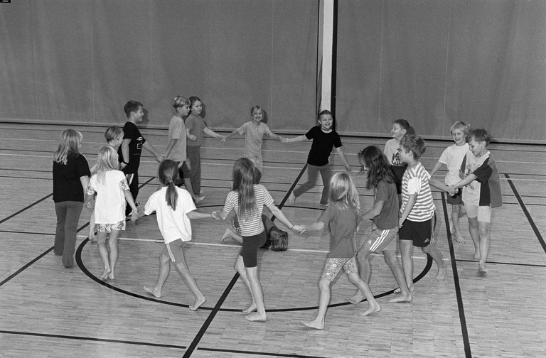 Lapsia leikkimässä piirileikkiä liikuntasalissa. Mustavalkoinen valokuva.