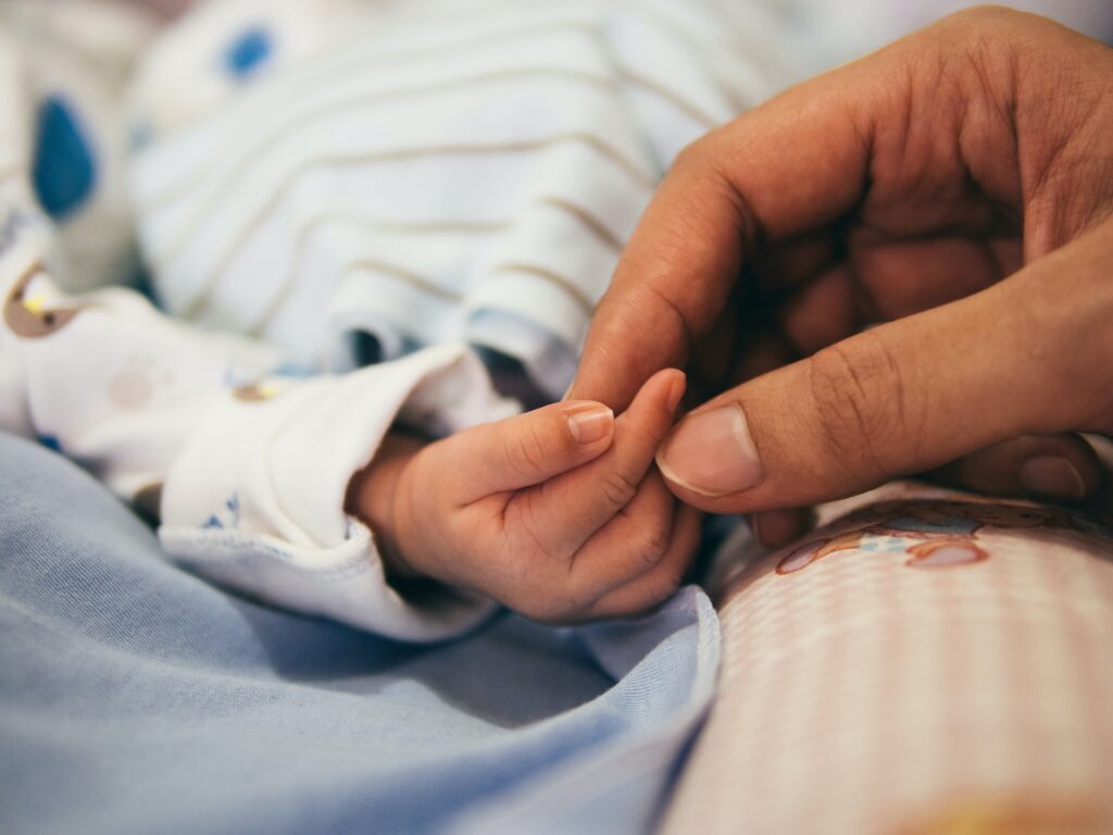Aikuinen pitää vastasyntynyttä vauvaa kädestä.