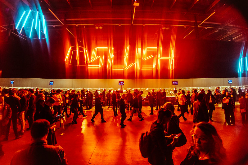 Väkijoukkoa Slush-tapahtumassa. Takaseinällä näkyy värivaloilla muodostettu teksti "Slush".