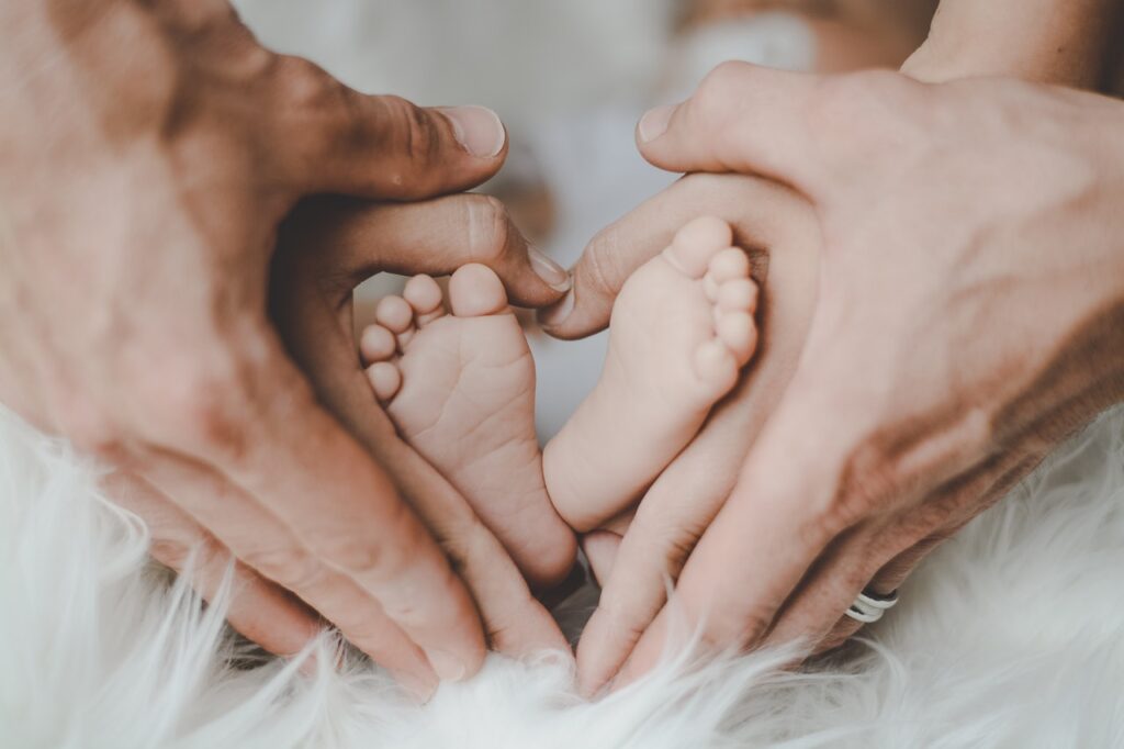 Kaksi aikuista muodostaa käsillään sydämen pienen vauvan jalkapohjien ympärille.