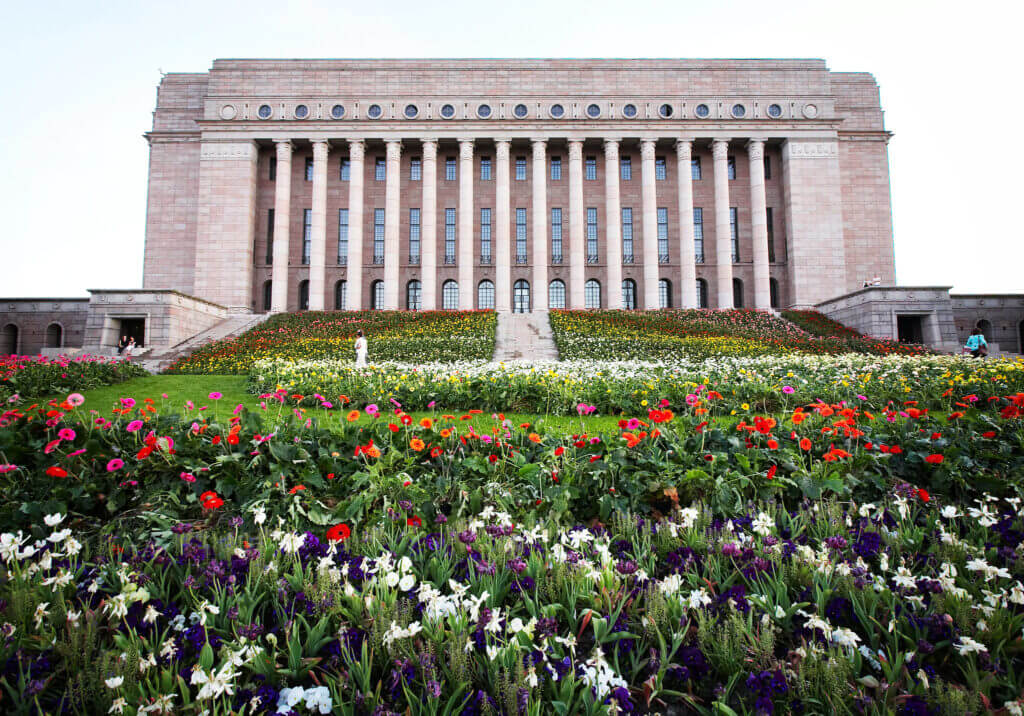 Suomen Eduskuntatalo, jonka portaille ja edustalle on istutettu kukkia. 