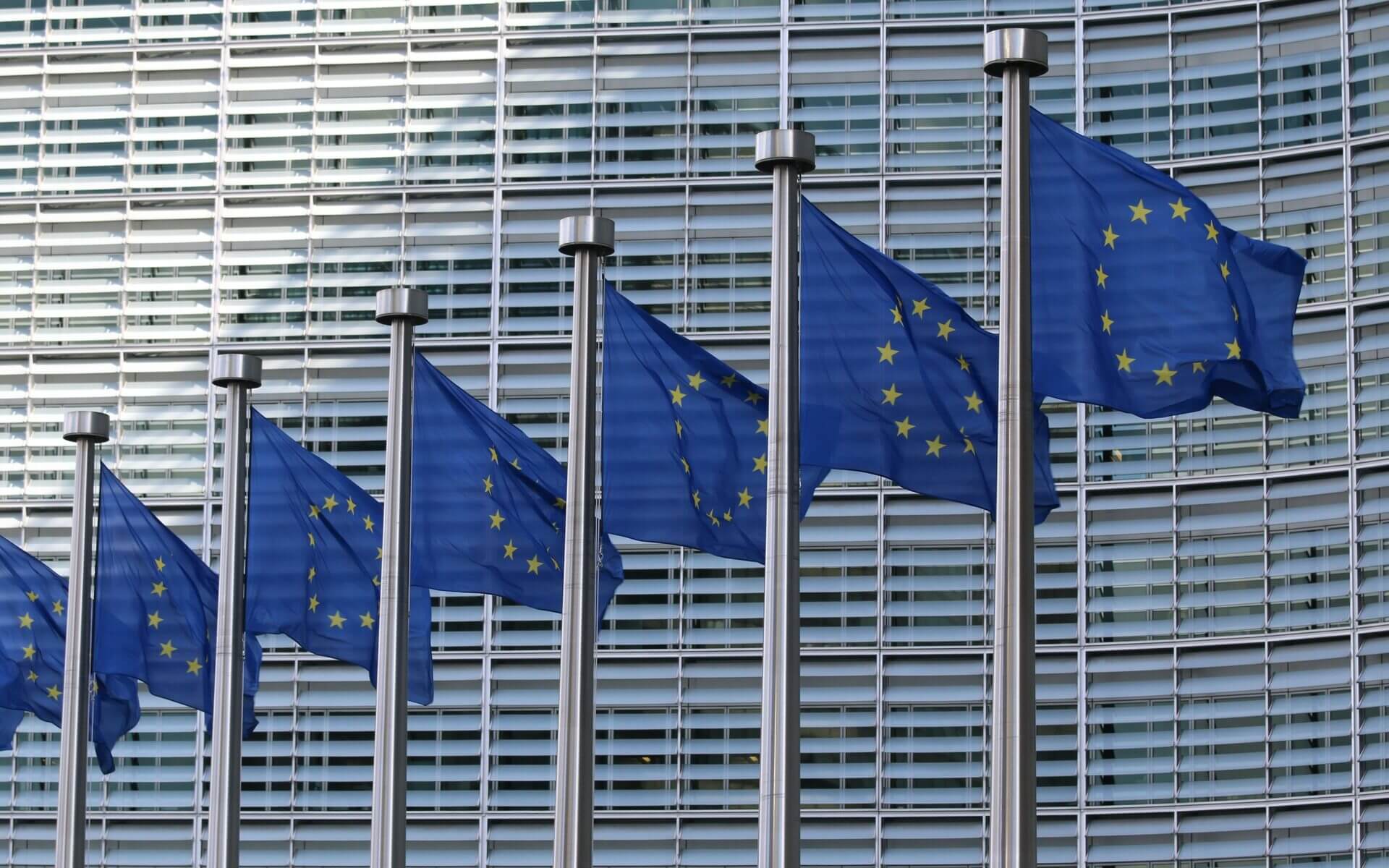 Seitsemän liehuvaa Euroopan unionin lippua harmaan rakennuksen edessä.