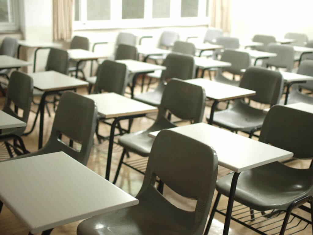 Näkymä tyhjään luokkahuoneeseen, jossa on valkoisia pulpetteja ja harmaita tuoleja.