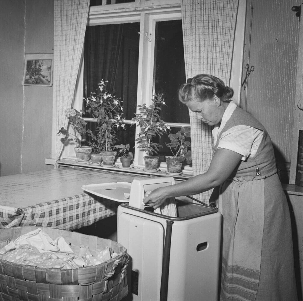 Naishahmo vääntämässä pyykkiä kuivaksi pulsaattorilla Parikkalassa 1953. Mustavalkoinen valokuva.