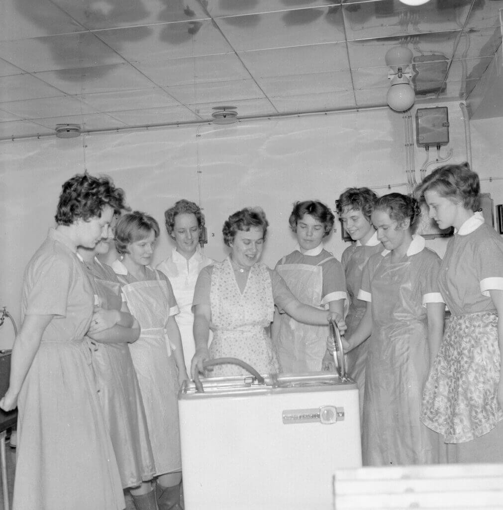 Naishahmoja katselemassa pyykinpesukonetta 1964. Mustavalkoinen valokuva.