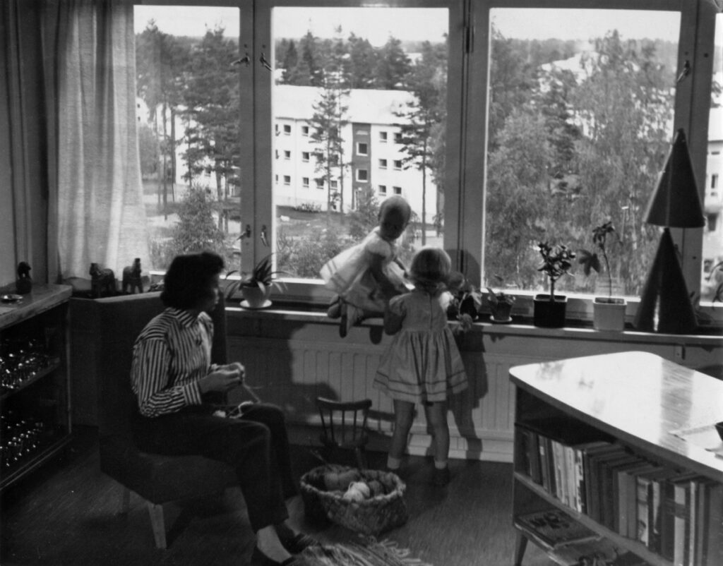 Perhe-elämää uudessa lähiössä. Todennäköisesti valokuvaaja Olavi Mannosen koti, Roihuvuorentie 18 A. Ikkunasta näkyy kerrostalo, Roihuvuorentie 9. mustavalkoinen