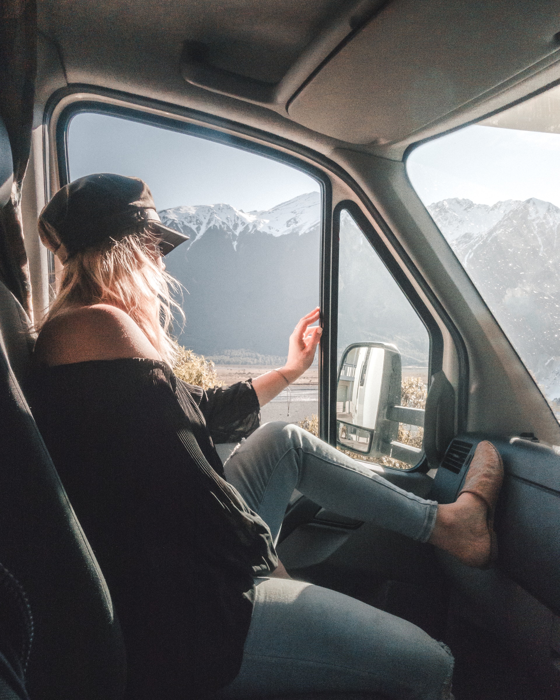 Nainen istuu pakettiauton etuosassa. Taustalla näkyy vuoria.