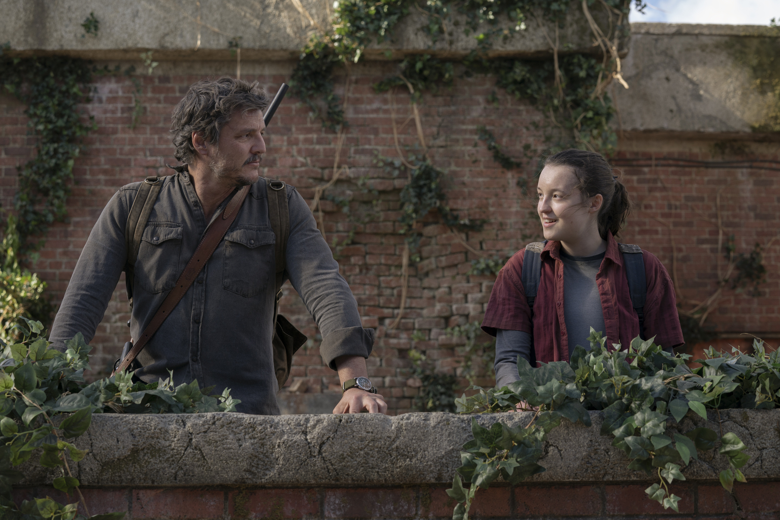 Valokuva The Last of Us -televisiosarjasta. Kuvassa vasemmalla Pedro Pascalin esittämä Joel katsoo Bella Ramseyn esittämää Ellietä tiilimuurin edustalla.