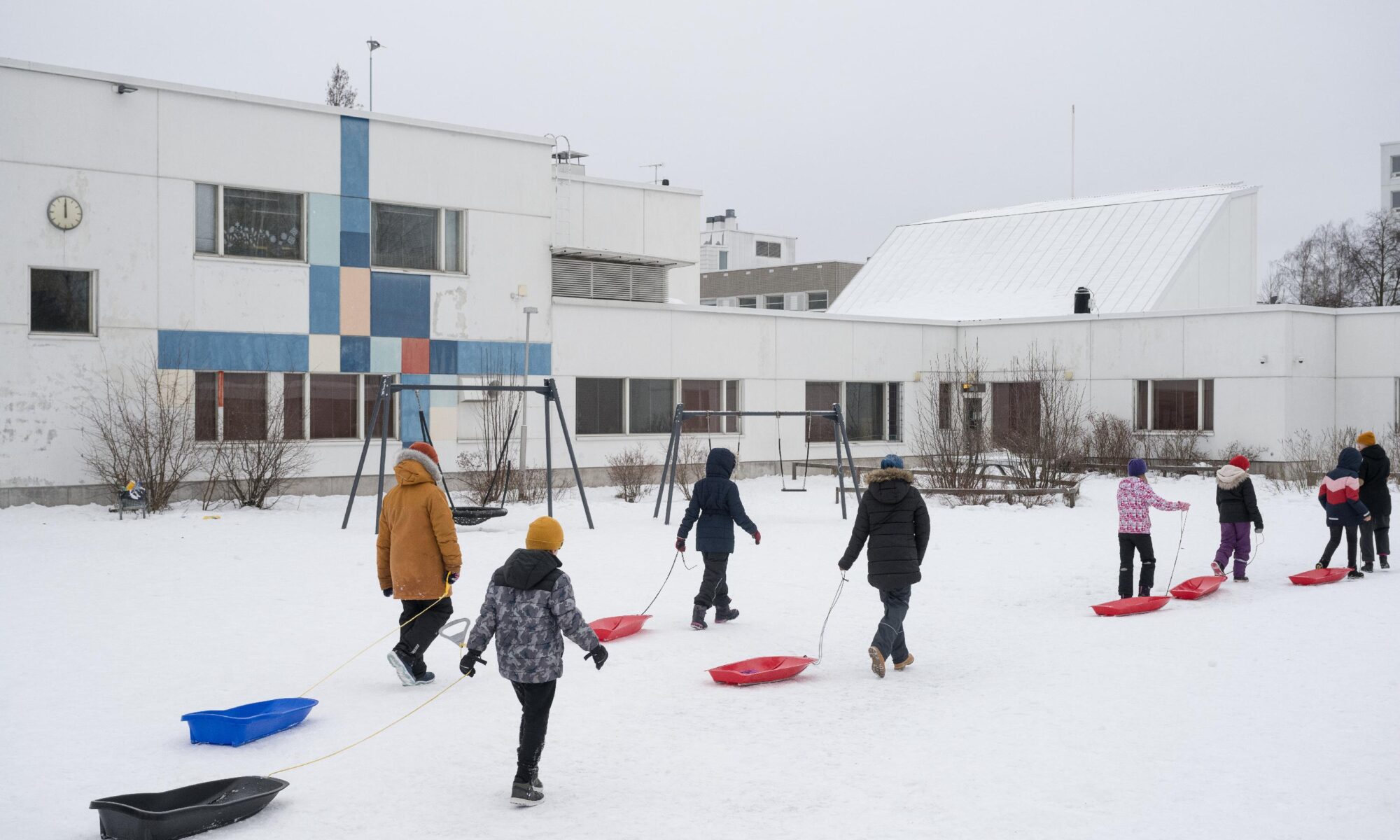Koululaiset vetävät pulkkia Merilahden peruskoulun Jaluspolun toimipisteen lumipeitteisessä pihassa.