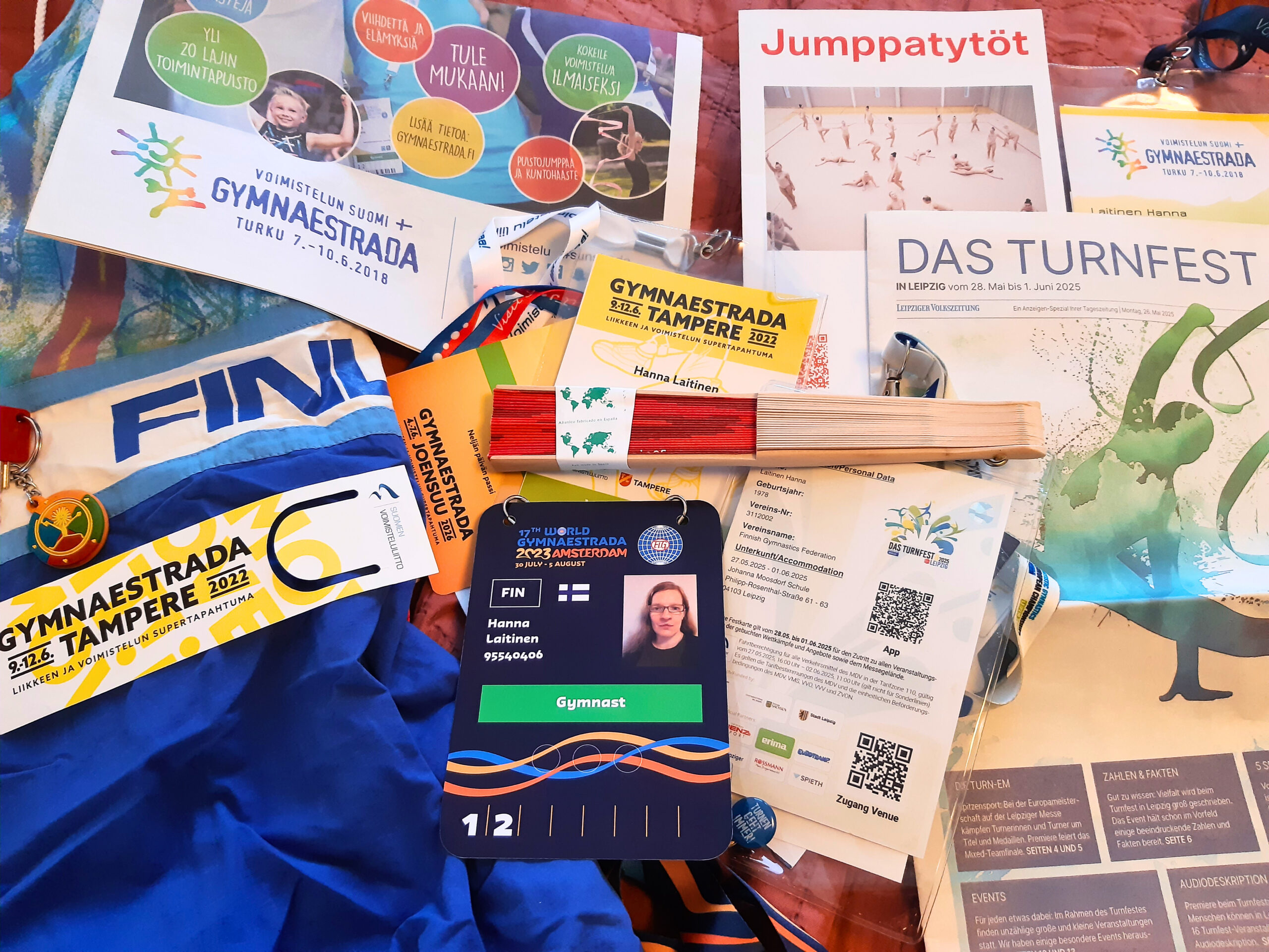 Kuvassa voimisteluun liittyvää tavaraa, kuten viuhka, Gymnaestradan esitteitä ja Hanna Laitisen voimistelijapasseja eri vuosien voimistelukilpailuista.