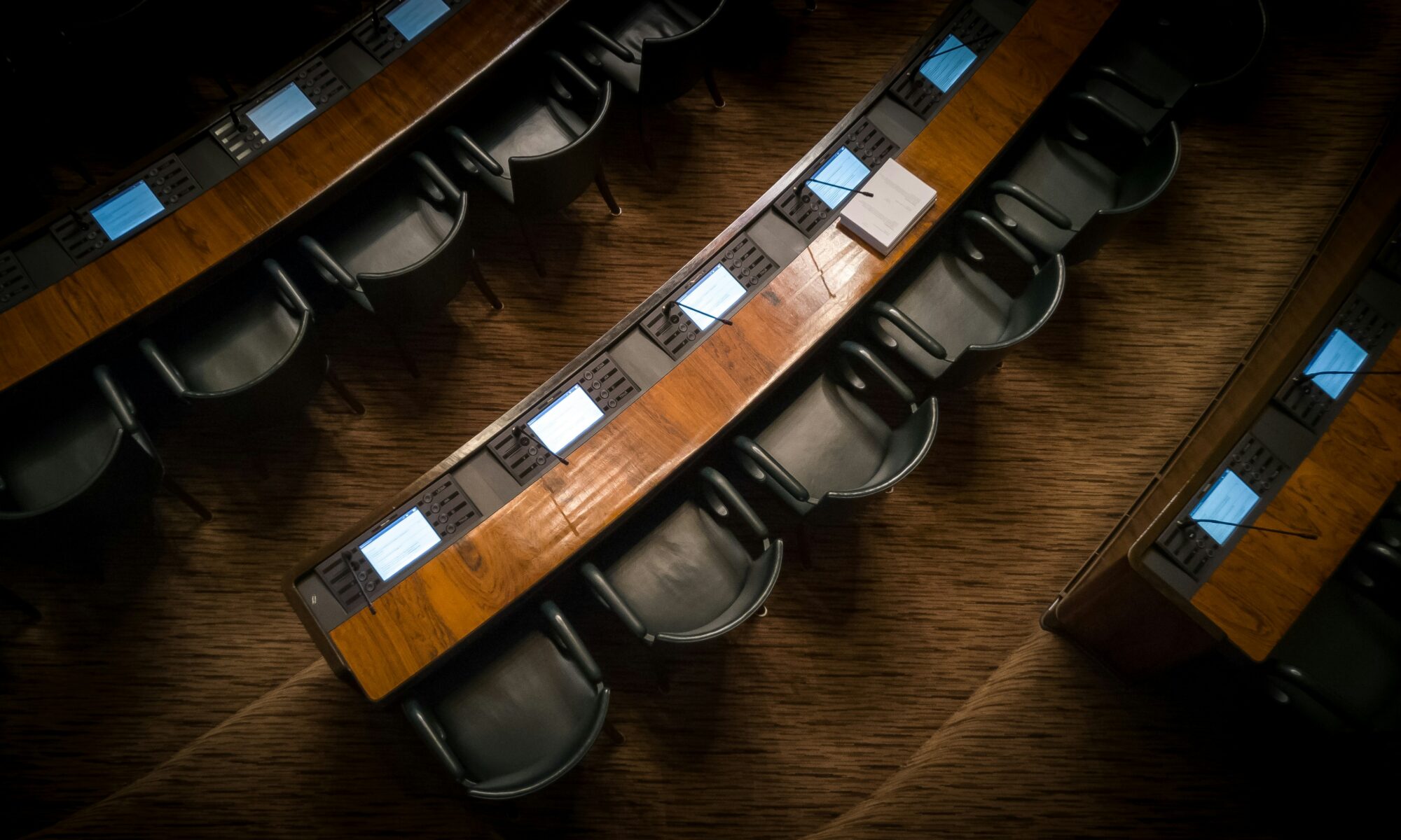 Kuva Eduskuntasalin lehtereiltä alaspäin, kansanedustajien pöytäpaikkoja tyhjänä. Kuvassa tumma valaistus.