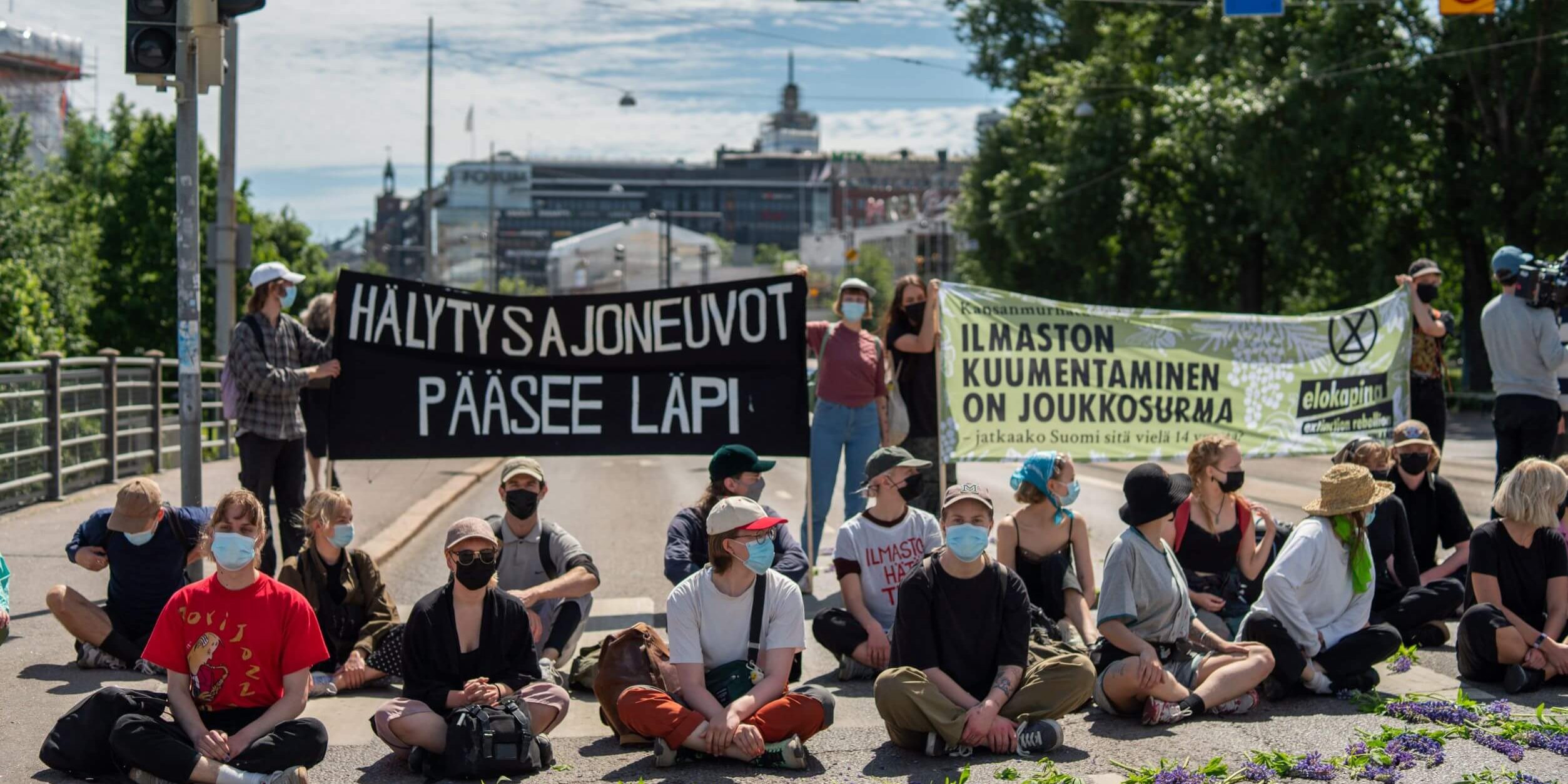 Mielenosoittajia istumassa ajoväylällä Elokapinan mielenosoituksessa.
