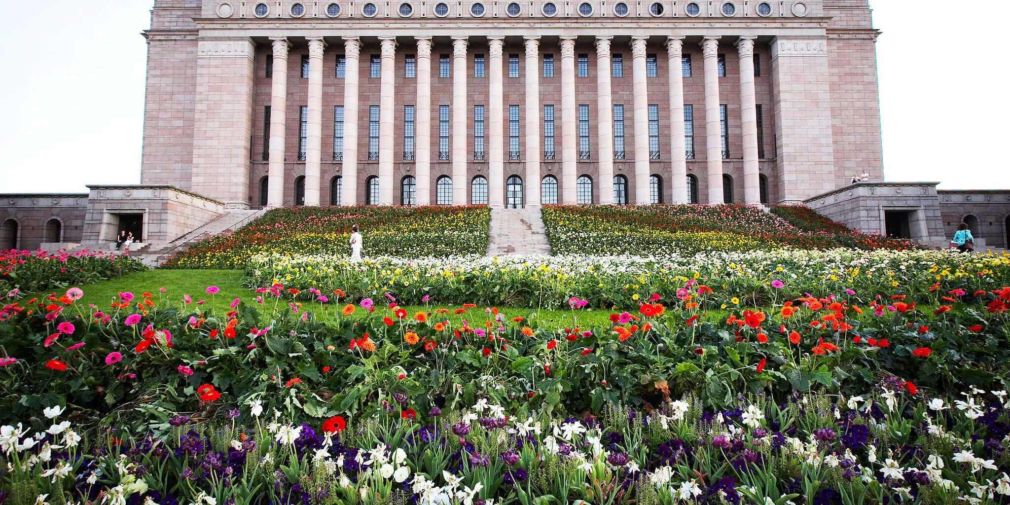 Suomen Eduskuntatalo, jonka portaille ja edustalle on istutettu kukkia.