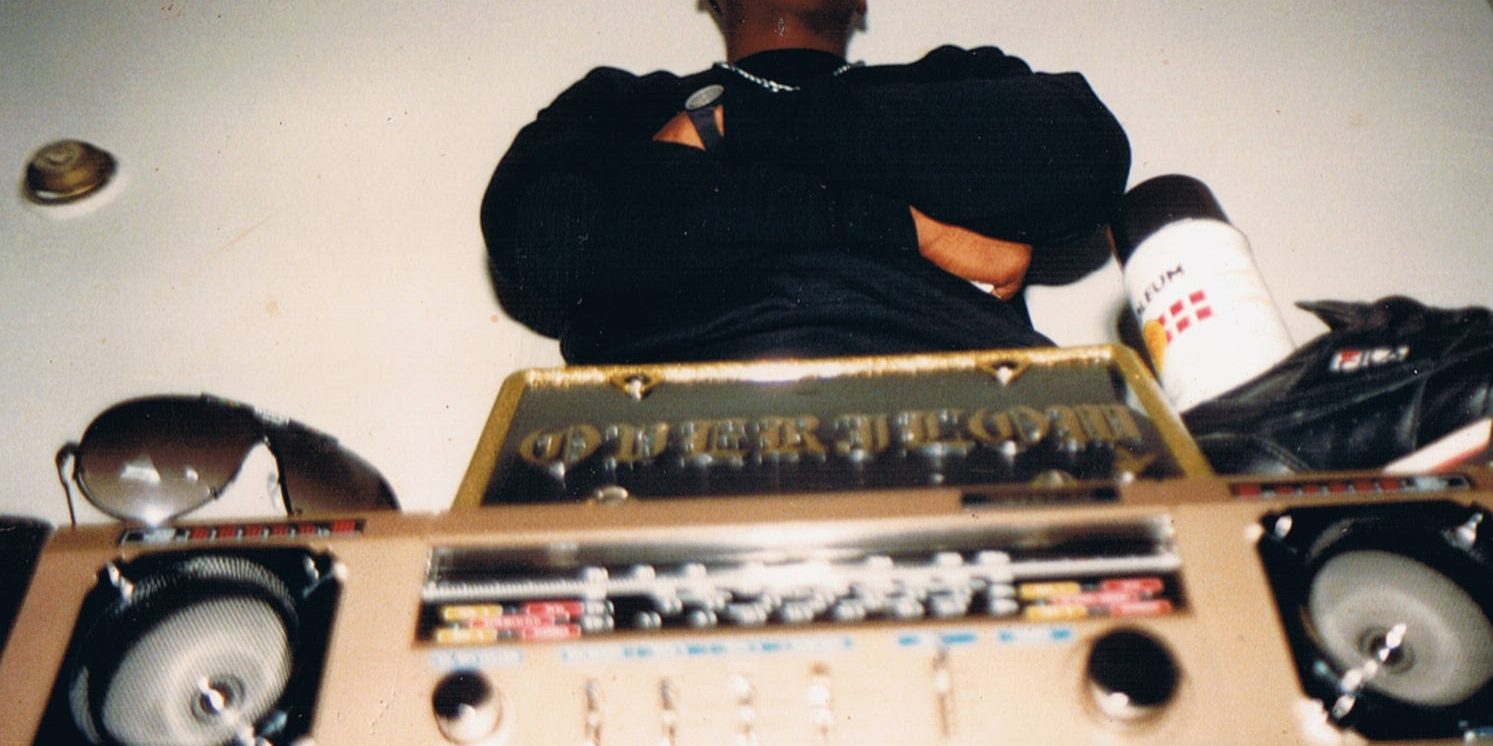1980-lukulainen kasettimankka etualalla. Taustalla mustaan paitaan ja lippalakkiin pukeutunut mies seisoo kädet puuskassa.