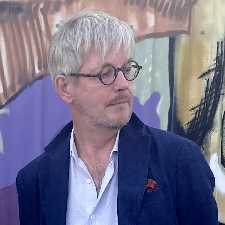 Professori Mikko Lagerspetz. Vaaleahiuksinen henkilö, jolla pyöreät, tummasankaiset silmälasit, tummansininen takki ja vaaleansininen kauluspaita.
