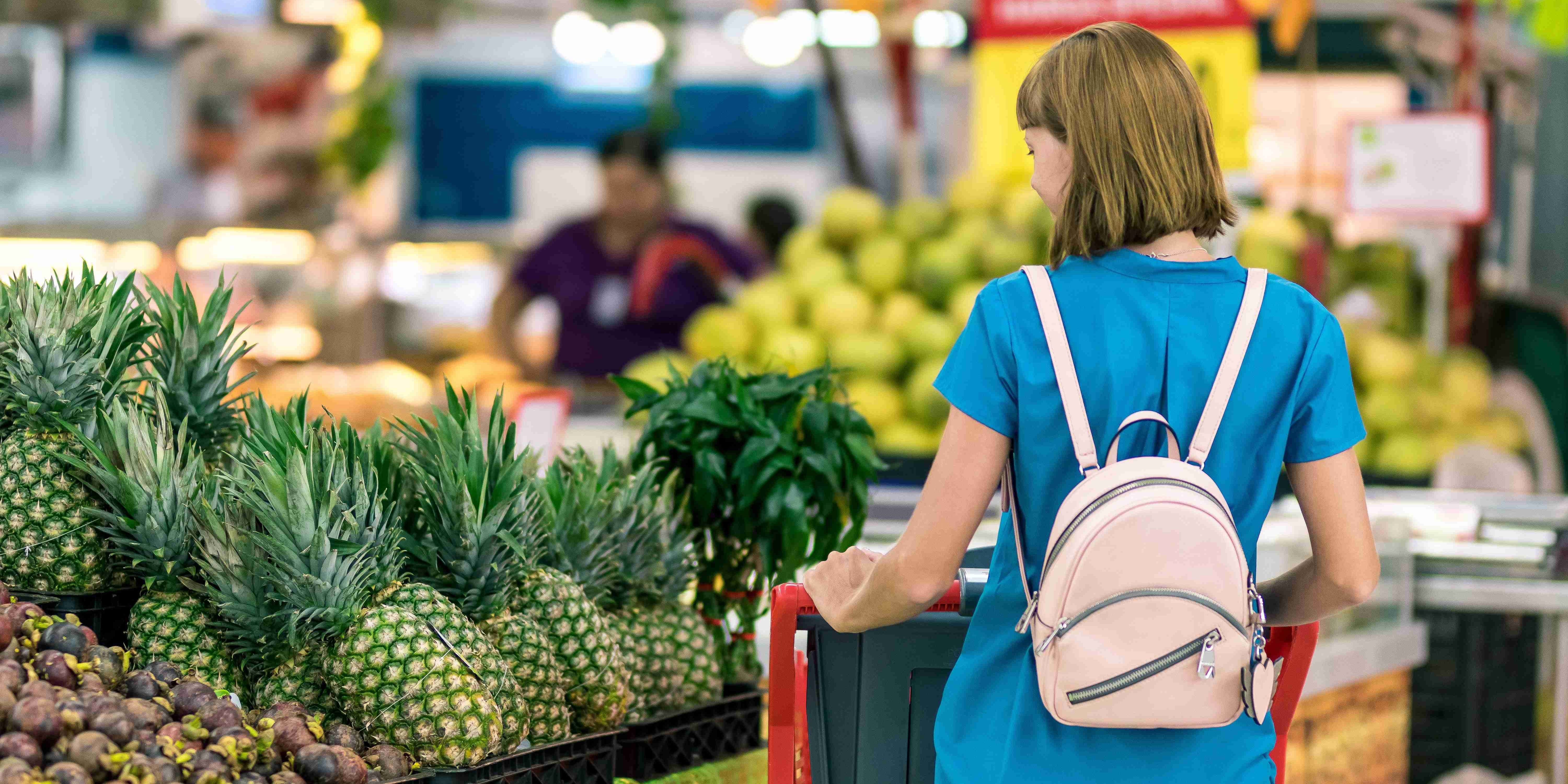 Nainen ostoskärryjen kanssa kaupan hedelmäosastolla.