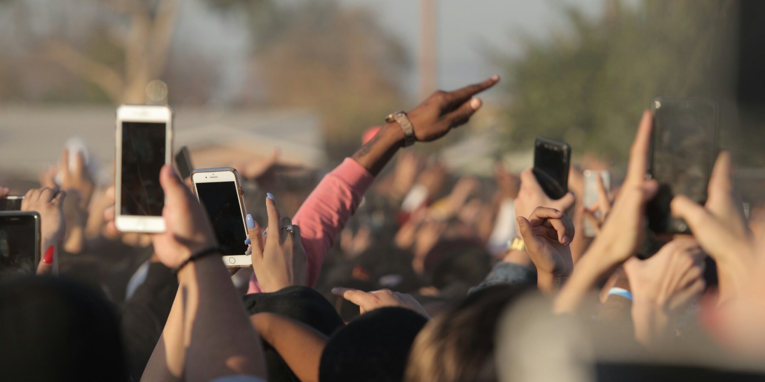 Kuva yleisöstä, jossa useilla ihmisillä on kädet ilmassa. Monet pitelevät kädessään älypuhelinta.