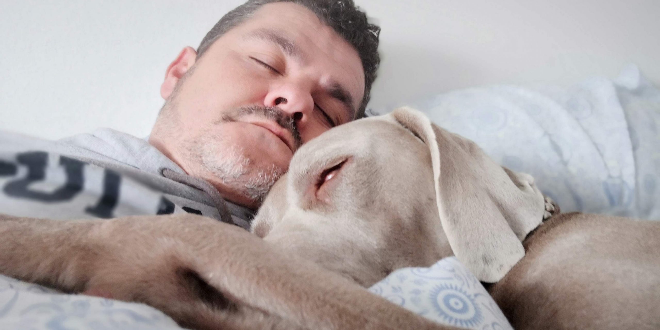 Mies nukkuu vaalea koira kainalossaan.