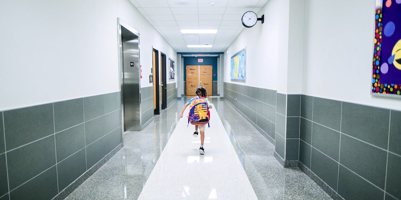 Lapsi juoksee koulun käytävää reppu selässään.